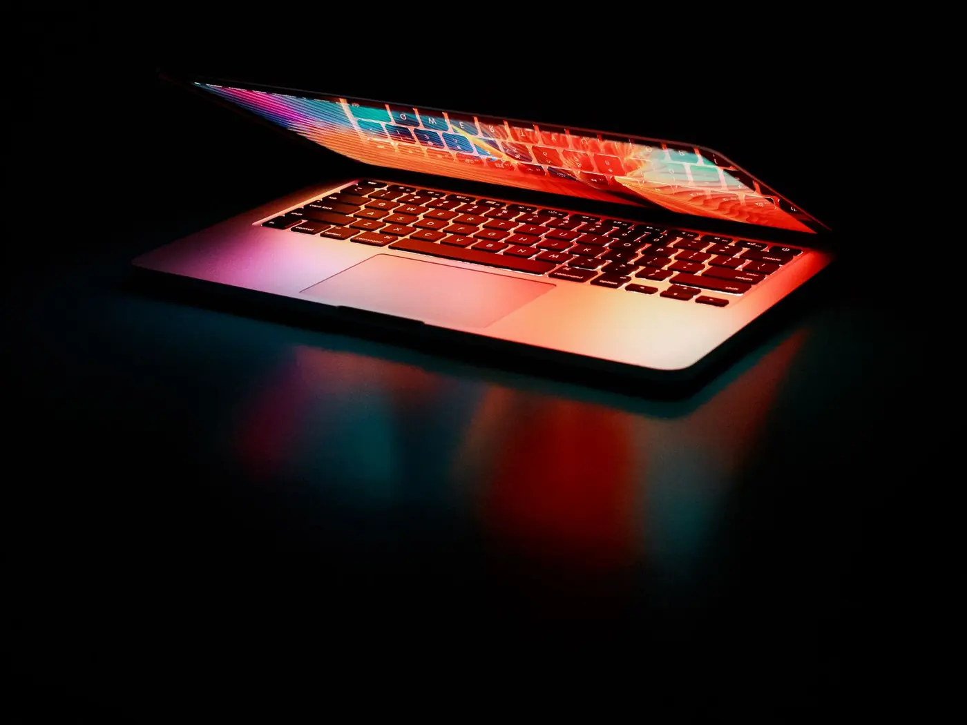Open silver laptop on a dark desk, colored monitor glow