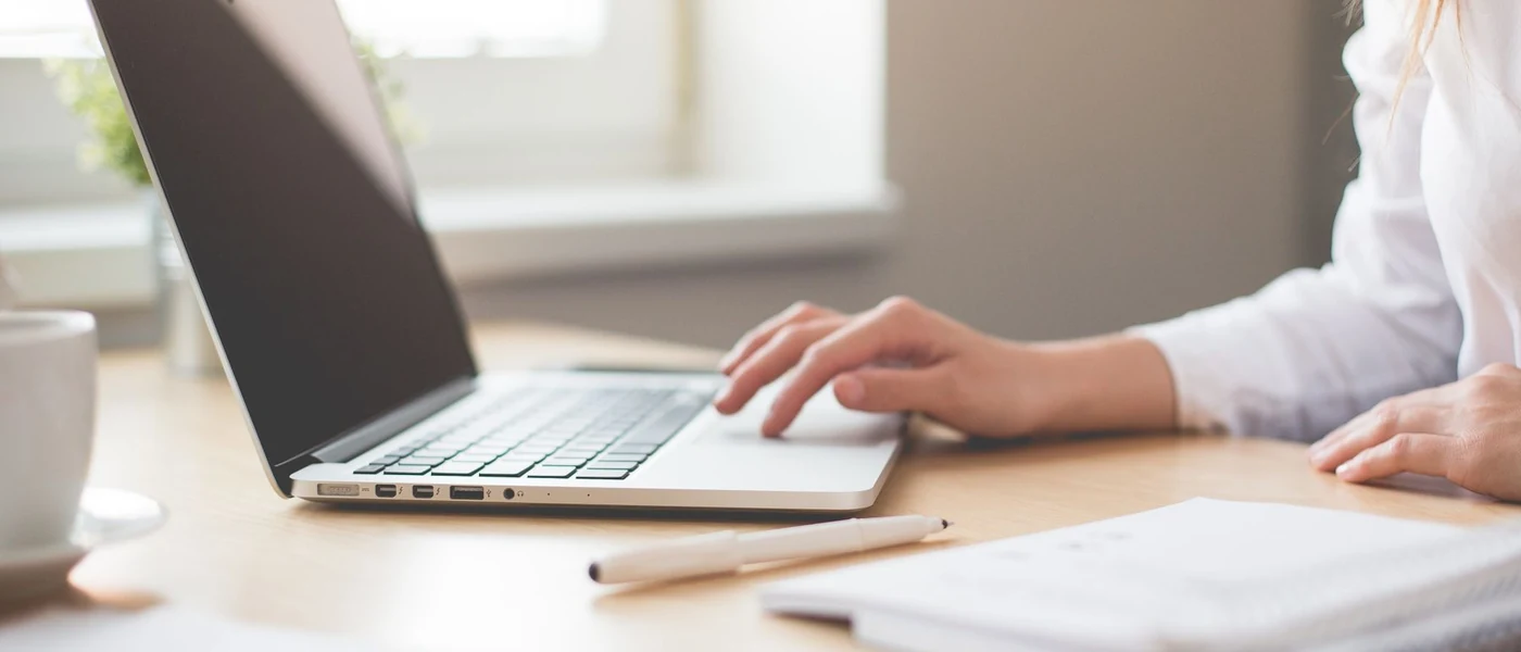 Person in a white shirt typing on a silver laptop at a desk. Not Fortnite.