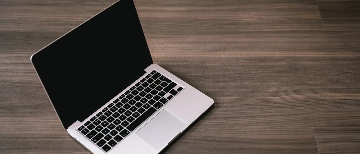 Open silver laptop with a black screen on a wooden table. Not Valorant.